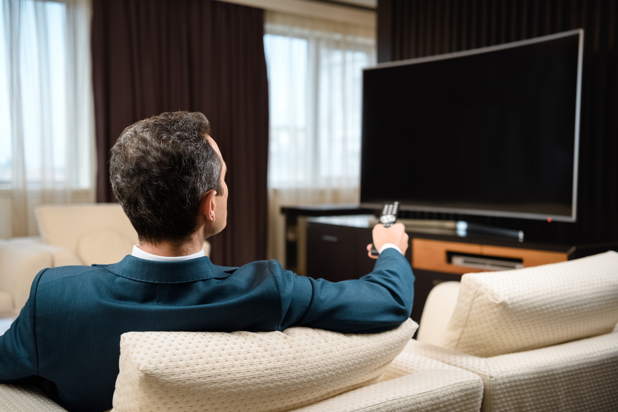 Businessman in formal suit sitting on sofa in hotel room and watching television