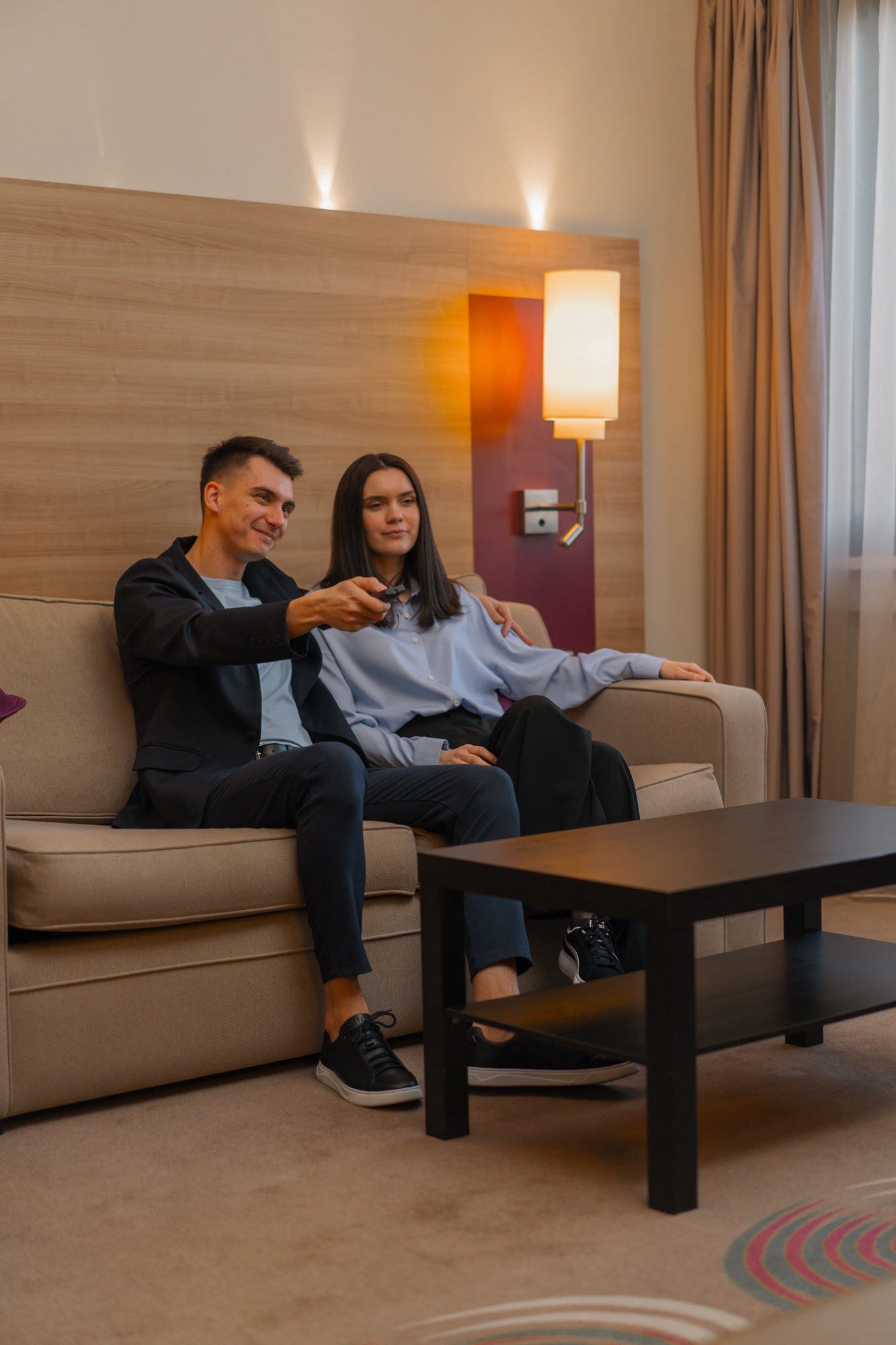 couple hotel room living room watching TV together Man takes remote control and switches channels